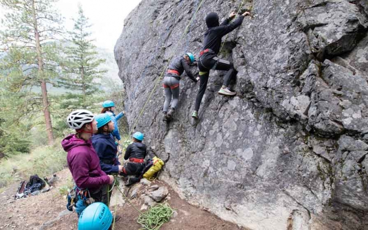 two students climb a rock wall while others look on from below